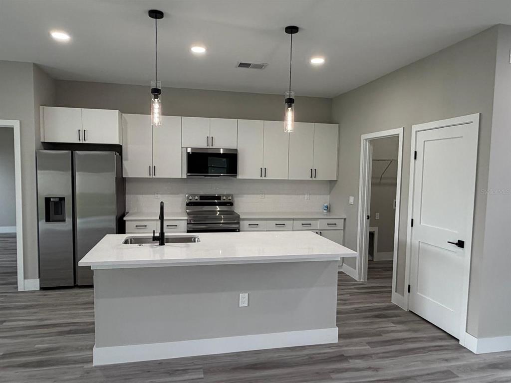 A modern kitchen with white cabinets and a central island overlooks an open living area — 7980 N PITCAIRN WAY, CITRUS SPRINGS, FL