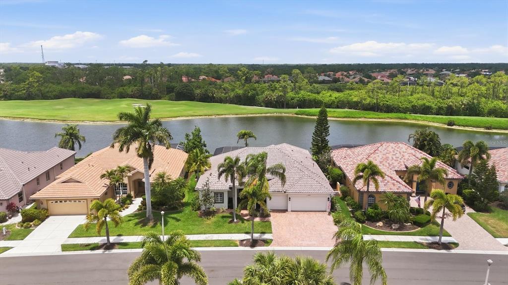 An aerial view shows three suburban houses with tile roofs facing a lake and golf course — 5184 WHITE IBIS DRIVE, NORTH PORT, FL