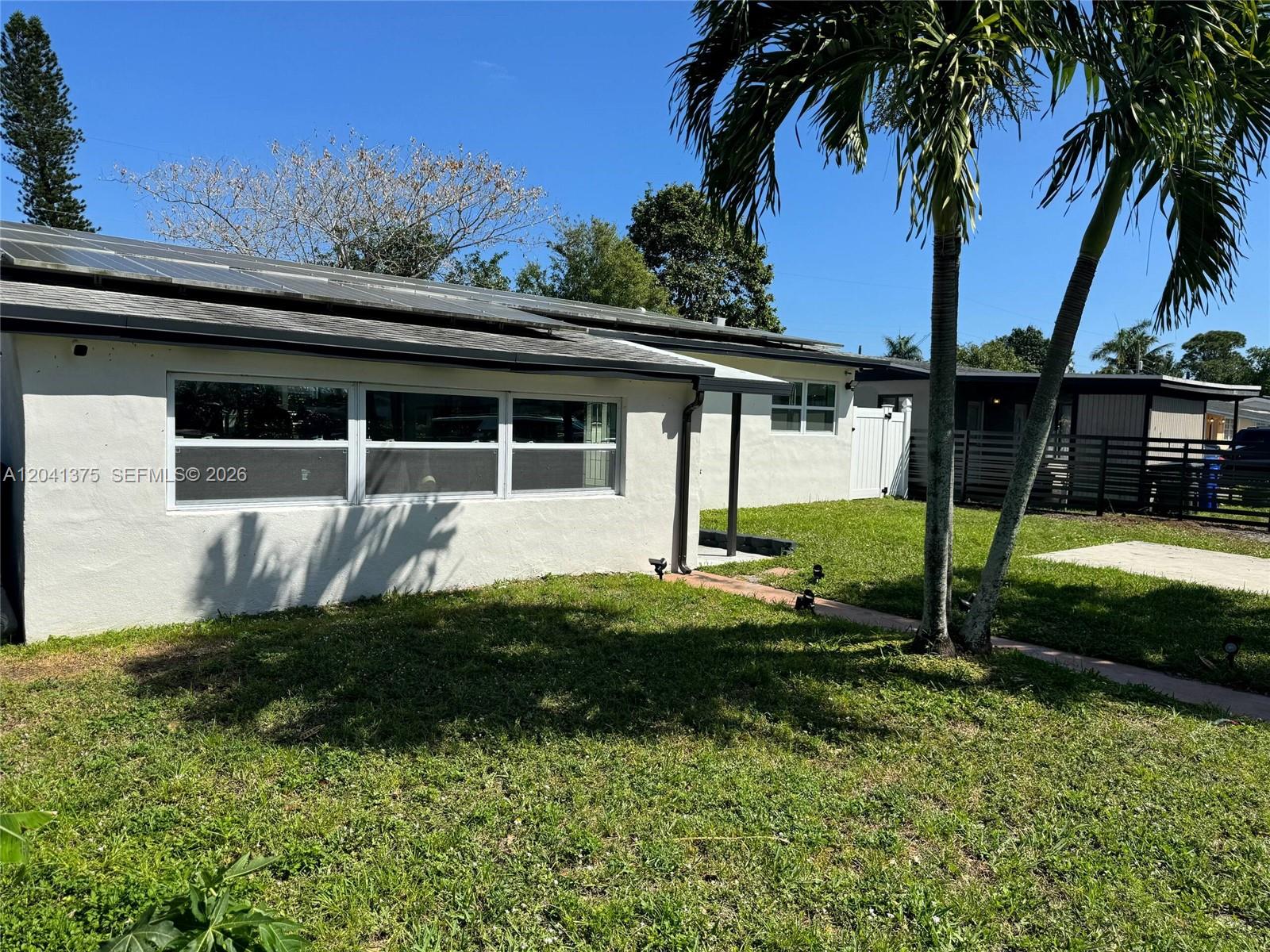 The exterior of a white house features solar panels on the roof and palm trees — 6453 Meade St, Hollywood FL 33024, HOLLYWOOD, FL