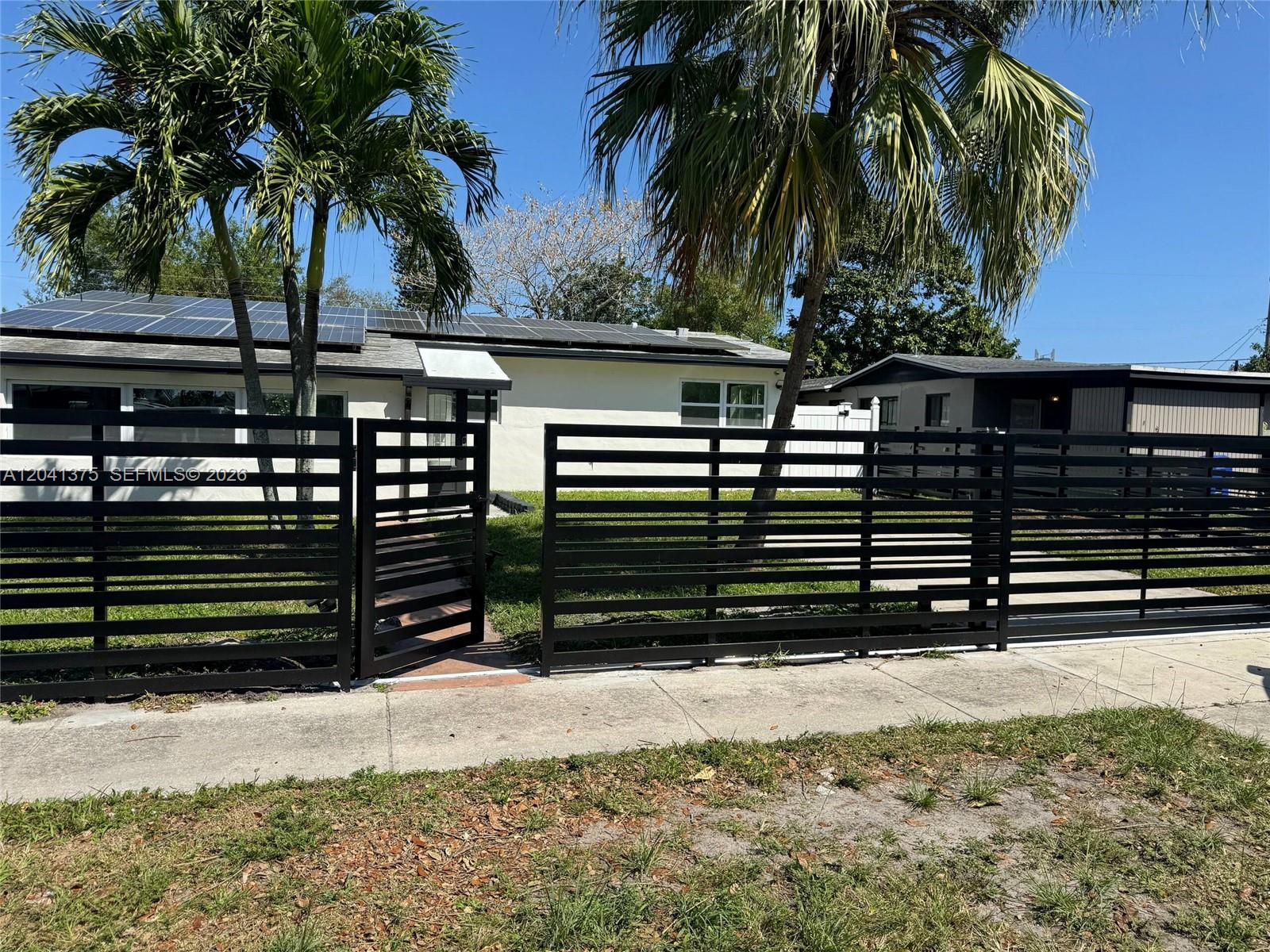 A single-story house with solar panels on the roof sits behind a modern horizontal fence — 6453 Meade St, Hollywood FL 33024, HOLLYWOOD, FL