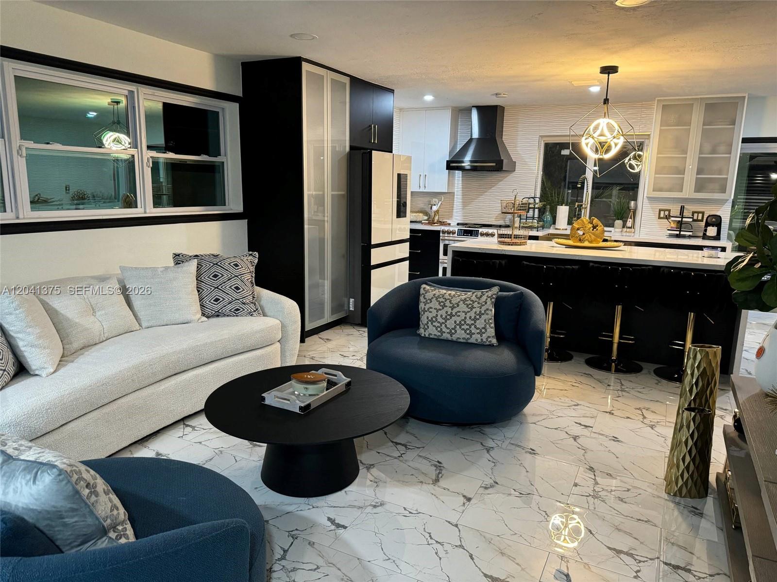 A modern open-concept living room and kitchen feature marble floors and black cabinetry — 6453 Meade St, Hollywood FL 33024, HOLLYWOOD, FL