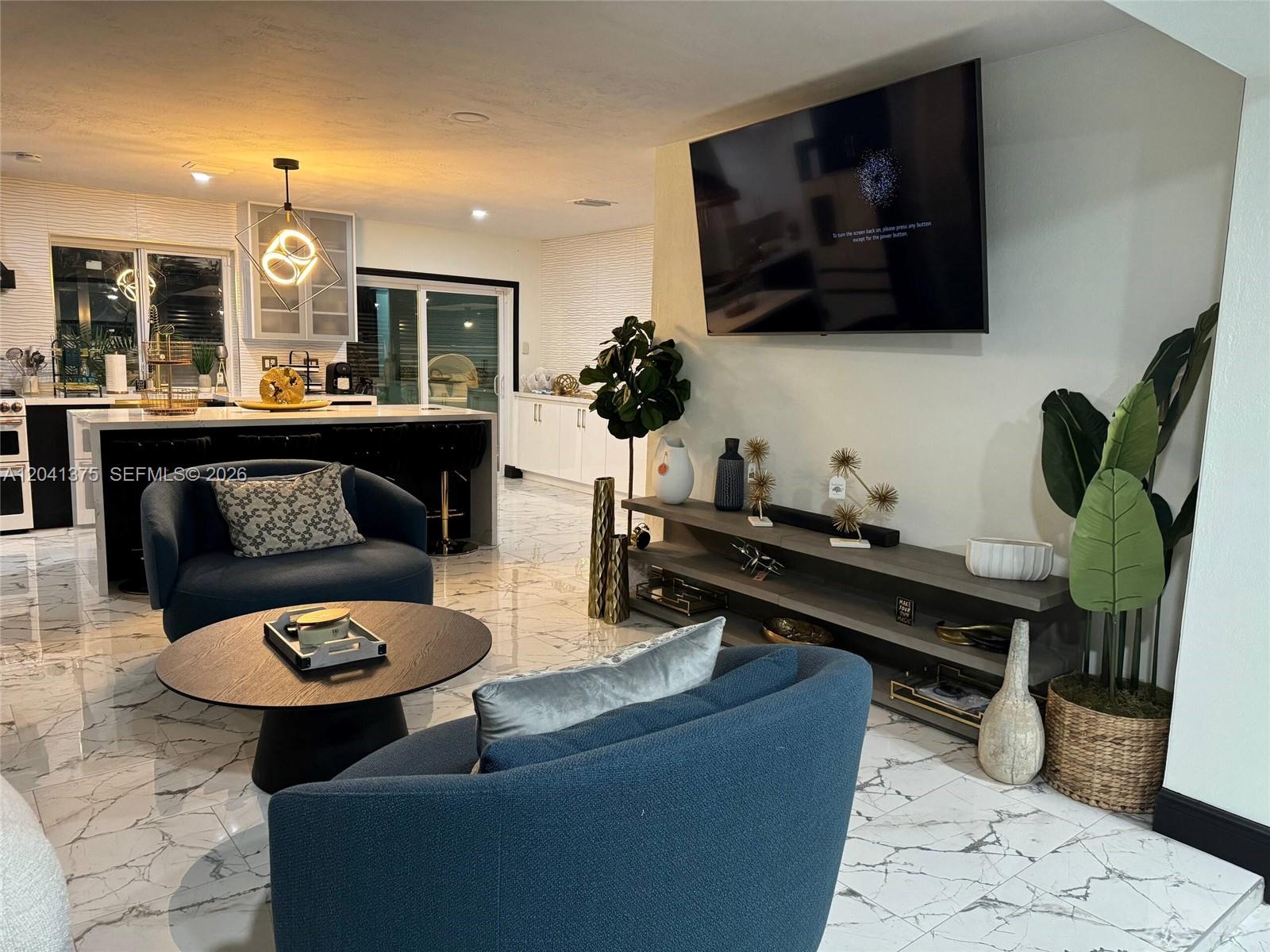 A living room with blue chairs, a round table, and a wall-mounted television — 6453 Meade St, Hollywood FL 33024, HOLLYWOOD, FL