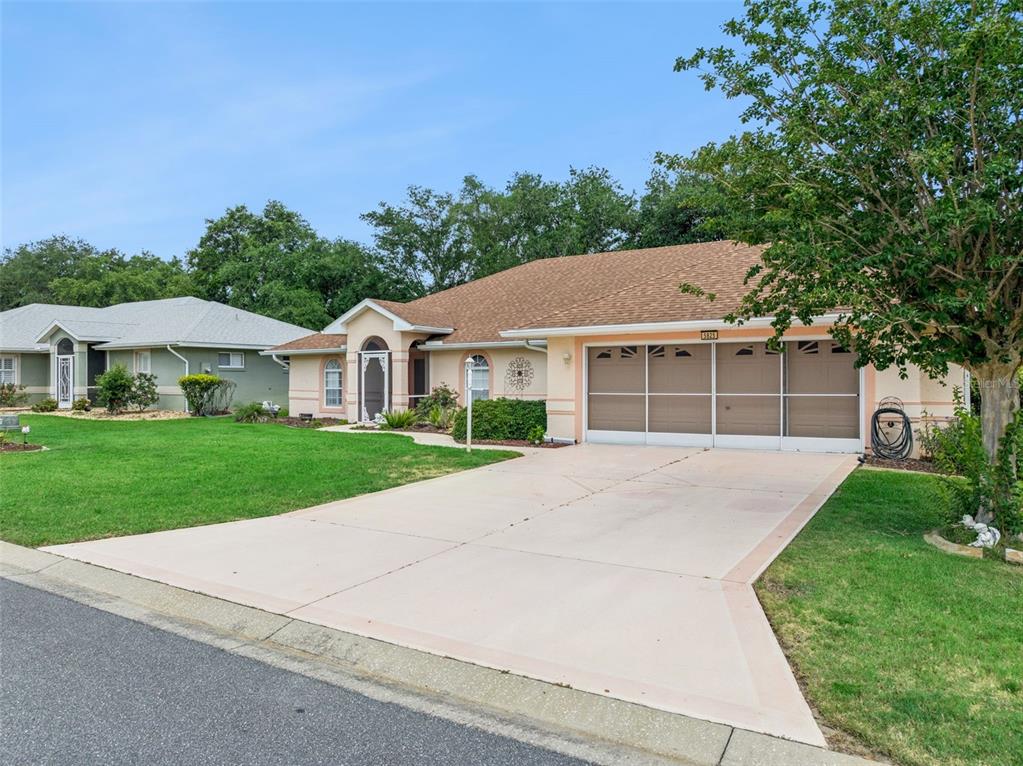 A single-story suburban house with a tan exterior, brown roof, and a two-car garage — 5825 PRINCESS CAROLINE PLACE, LEESBURG, FL