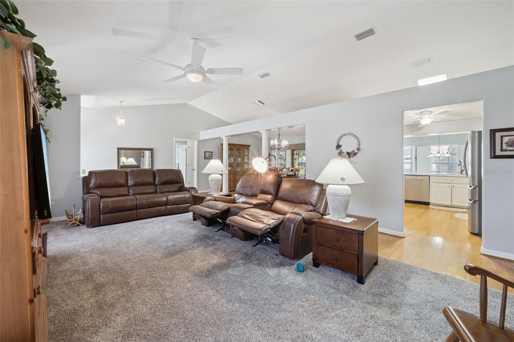 A living room features gray carpeting, brown leather reclining furniture, and an open kitchen view — 5825 PRINCESS CAROLINE PLACE, LEESBURG, FL