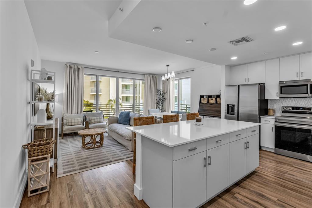 An open-concept kitchen with a white island overlooks a living area with wood-look flooring — 1703 N TAMIAMI TRAIL UNIT 211, SARASOTA, FL