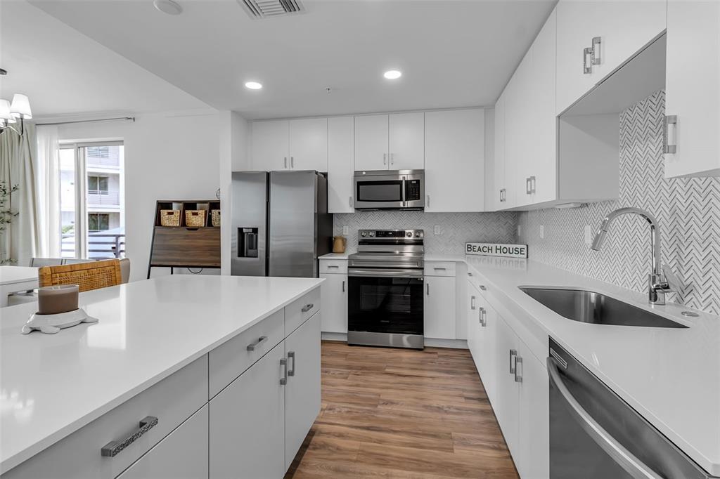 A modern kitchen features white cabinetry, stainless steel appliances, a quartz island, and herringbone backsplash — 1703 N TAMIAMI TRAIL UNIT 211, SARASOTA, FL