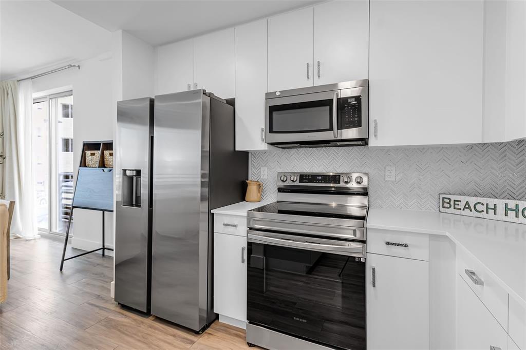 A modern kitchen features white cabinets, stainless steel appliances, and a herringbone tile backsplash — 1703 N TAMIAMI TRAIL UNIT 211, SARASOTA, FL