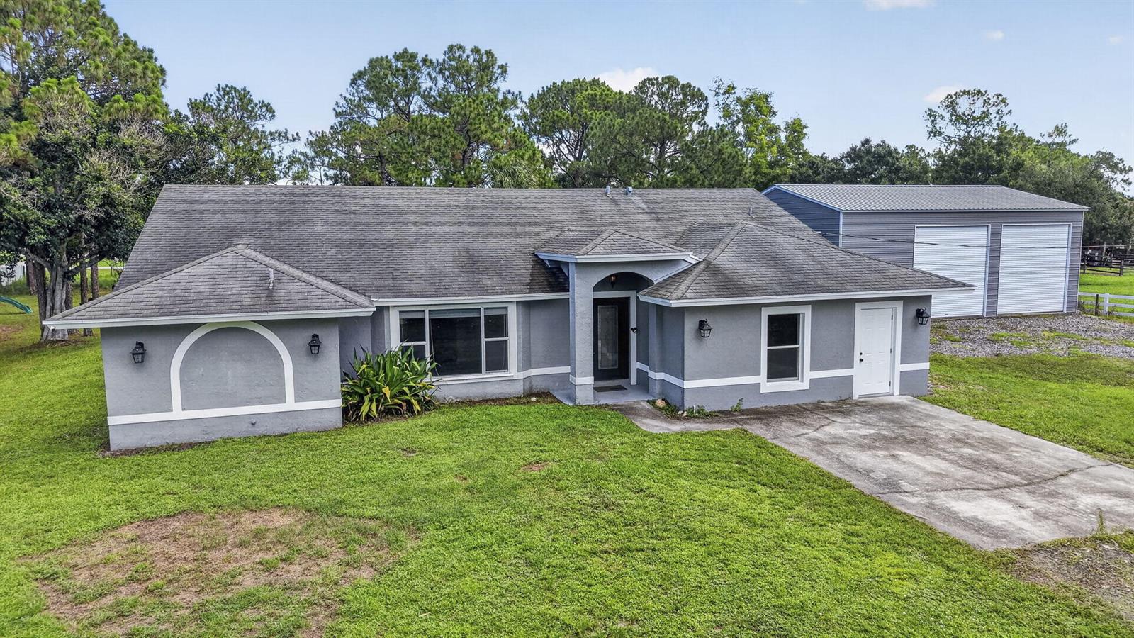 A gray single-story house with a detached metal garage sits on a grassy lot — 14935 89th Place N, Loxahatchee FL 33470, LOXAHATCHEE, FL