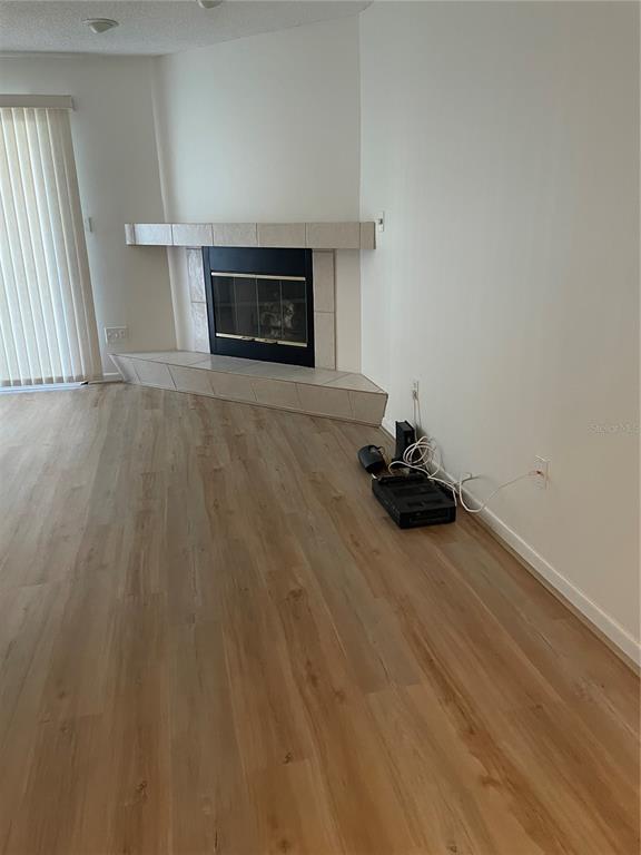 A living room features light wood-look flooring, white walls, and a corner fireplace with tile — 745 PINELLAS BAYWAY S UNIT 105, ST PETERSBURG, FL