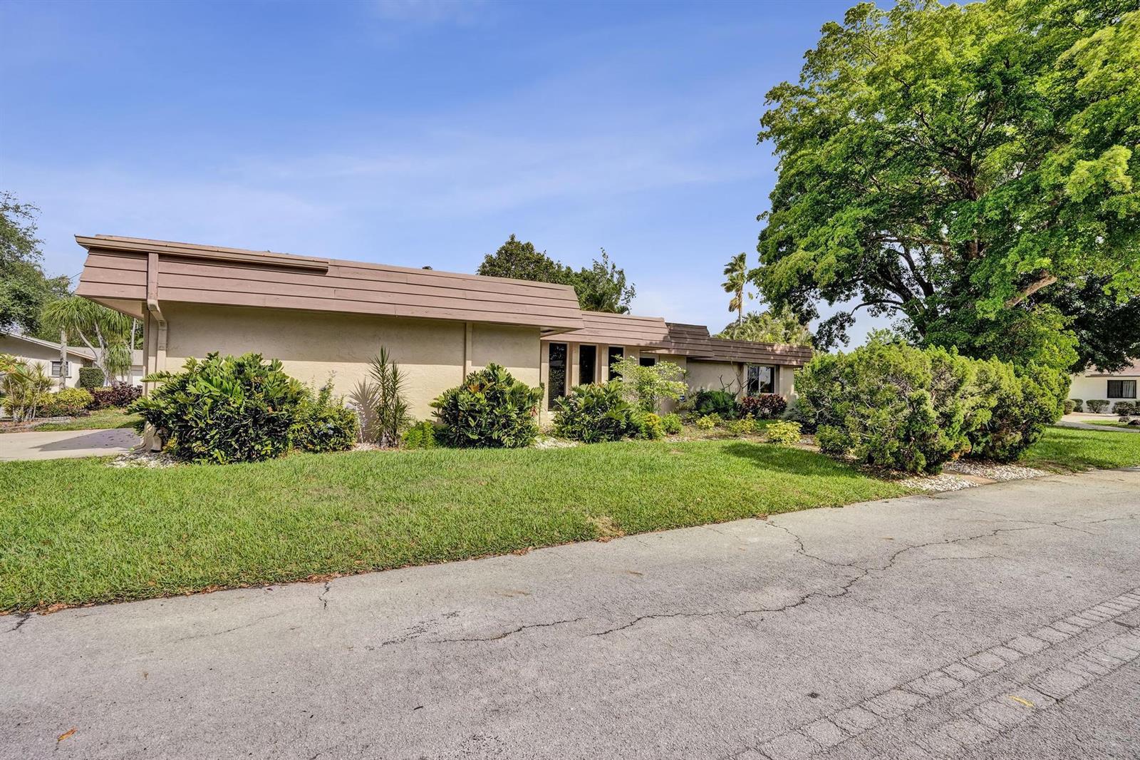 A single-story house with a brown flat roof and tan stucco exterior sits behind landscaping — 6207 Jacaranda Circle, Tamarac FL 33319, TAMARAC, FL