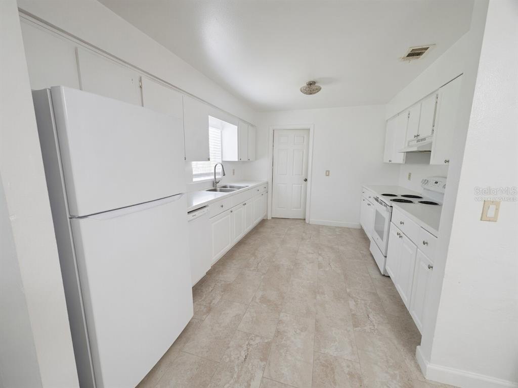 A white kitchen features white cabinetry, a refrigerator, a stove, and light-colored tile flooring — 31 DEACON JONES BOULEVARD UNIT A & B, ORLANDO, FL