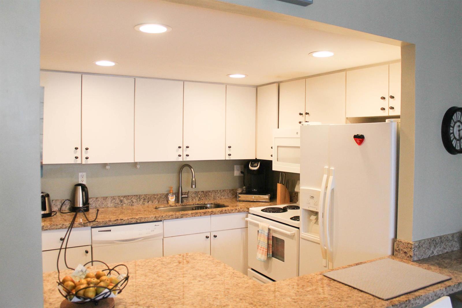 A kitchen features white cabinets, granite countertops, a white refrigerator, and a stainless steel sink — 1830 Embassy Drive # 306, West Palm Beach FL 33401, WEST PALM BEACH, FL