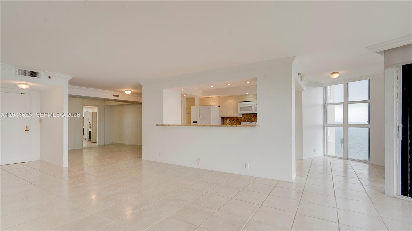 An open-concept living area features light tile flooring, a kitchen pass-through, and floor-to-ceiling windows — 4000 Towerside Ter # 908, Miami FL 33138, MIAMI, FL