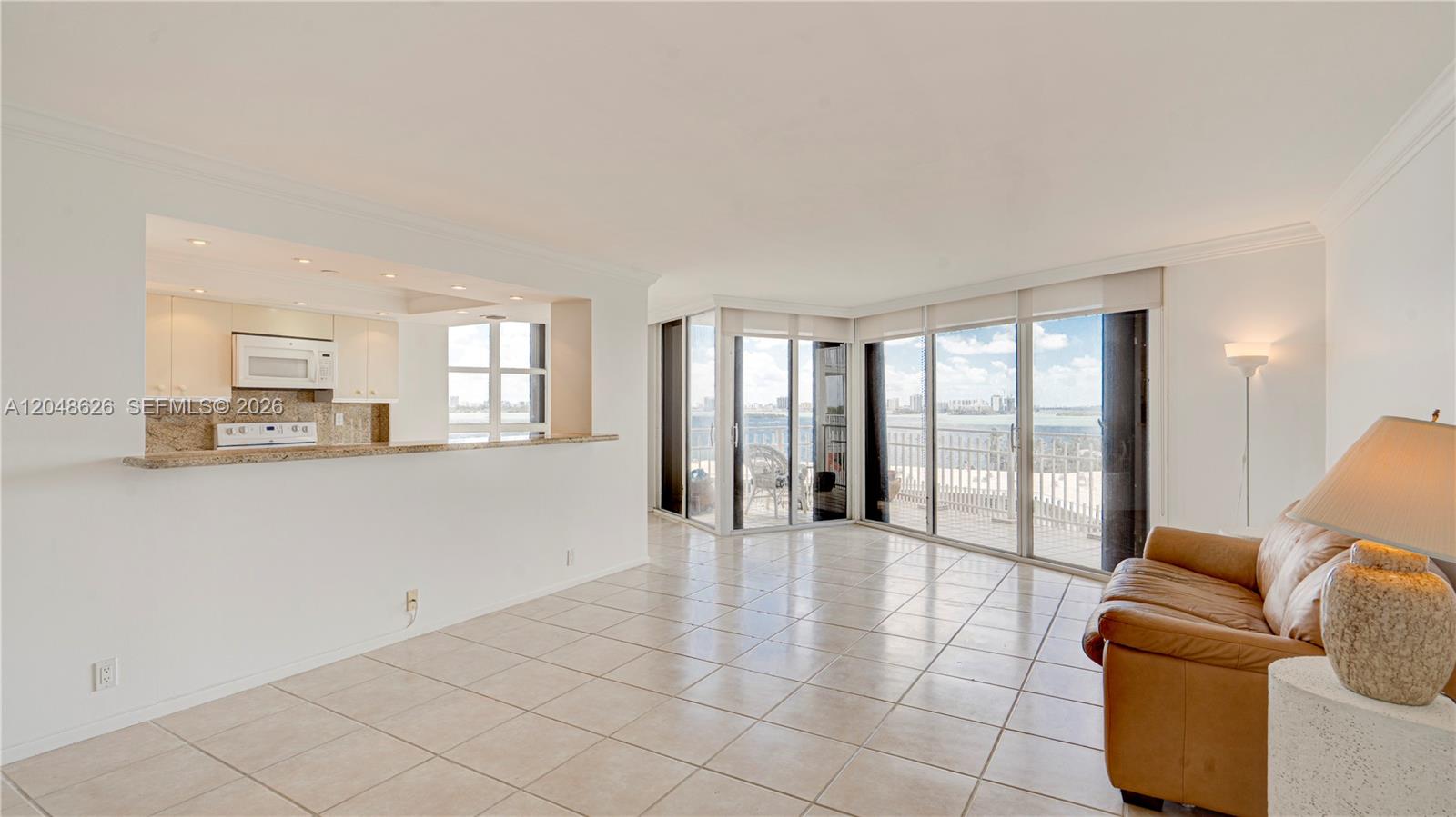An open-concept living area features tile flooring, a kitchen pass-through, and floor-to-ceiling balcony windows — 4000 Towerside Ter # 908, Miami FL 33138, MIAMI, FL