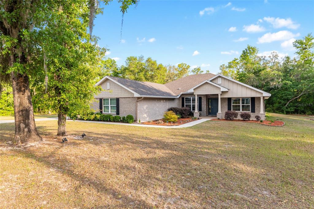 A single-story brick house with a covered entryway sits on a grassy, wooded lot — 8179 NE 8TH PLACE, HIGH SPRINGS, FL