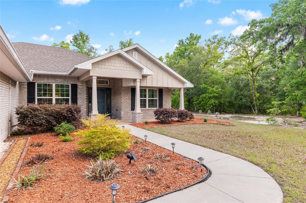 A single-story brick house with a covered entryway, shingled roof, and landscaped front yard — 8179 NE 8TH PLACE, HIGH SPRINGS, FL