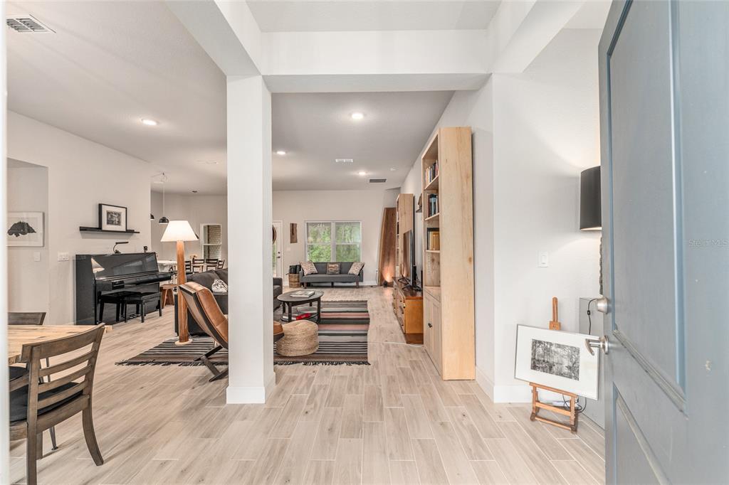 An open-concept living area features light wood-look tile flooring, a piano, and a tall bookshelf — 8179 NE 8TH PLACE, HIGH SPRINGS, FL