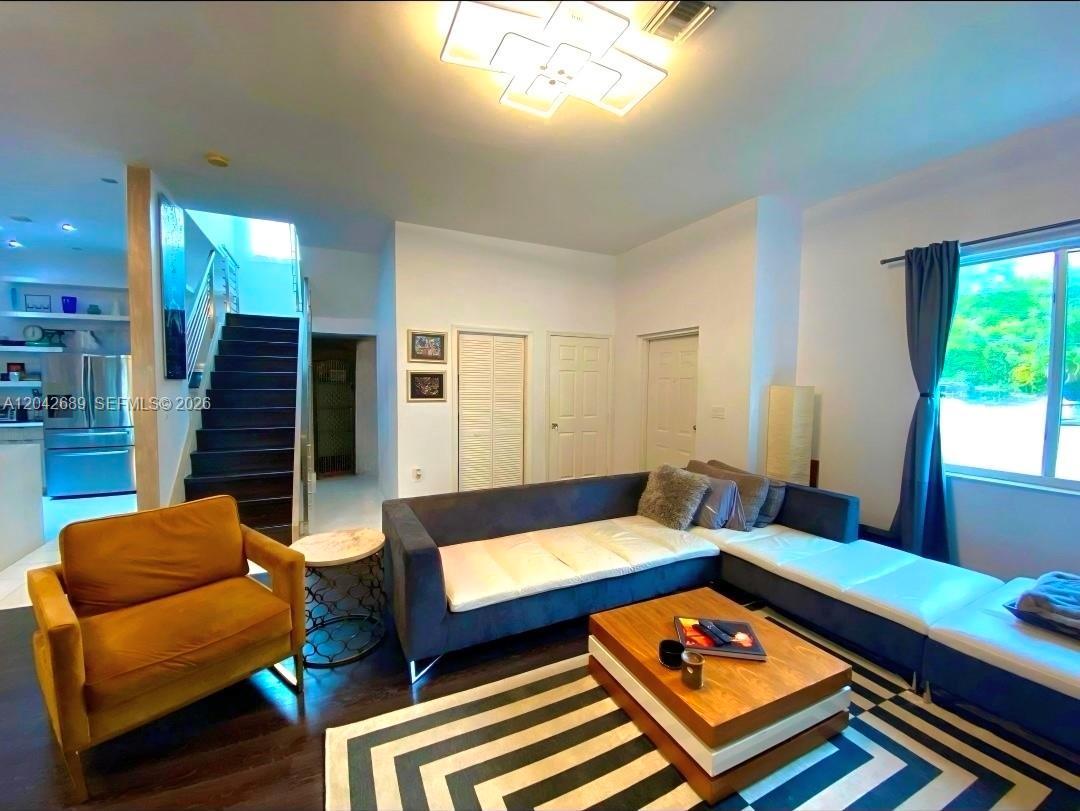 A living room features a dark sectional sofa, a mustard armchair, and a wooden staircase — 2732 SW 26 St # 2732, Miami FL 33133, MIAMI, FL