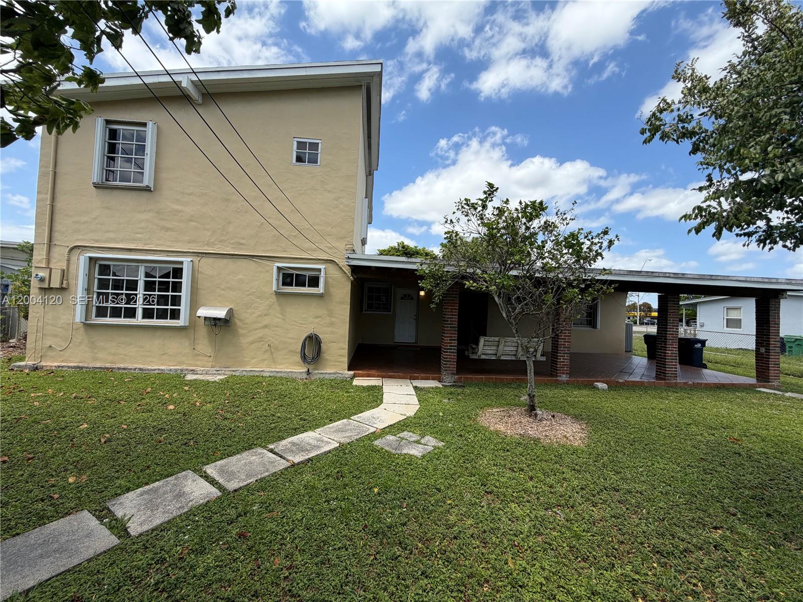 A two-story tan house features a covered porch, a stone walkway, and a small tree — 10910 SW 40th St, Miami FL 33165, MIAMI, FL