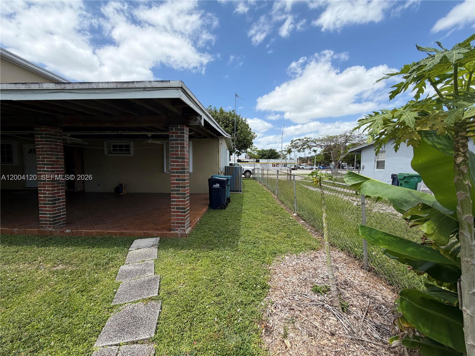 A covered patio with brick columns overlooks a grassy yard enclosed by a chain-link fence — 10910 SW 40th St, Miami FL 33165, MIAMI, FL