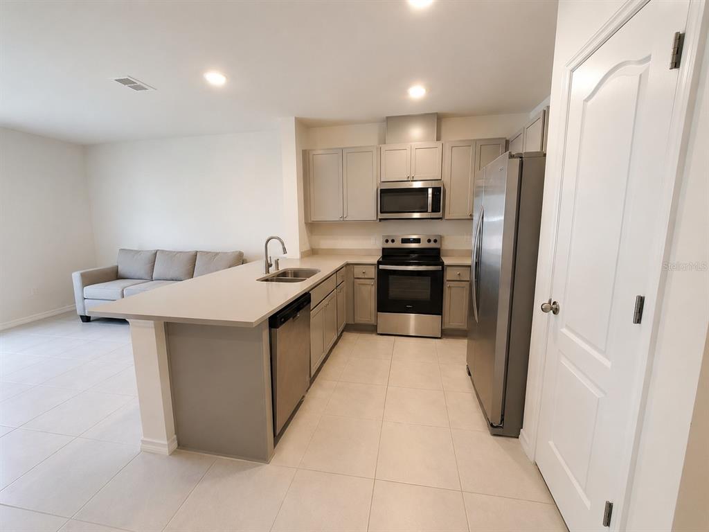 A kitchen with stainless steel appliances, gray cabinets, and a peninsula island overlooks a living area — 2393 PENGUIN BOULEVARD, DAVENPORT, FL