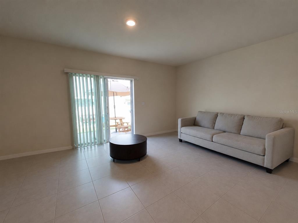 A living room features light tile flooring, a beige sofa, a coffee table, and sliding doors — 2393 PENGUIN BOULEVARD, DAVENPORT, FL