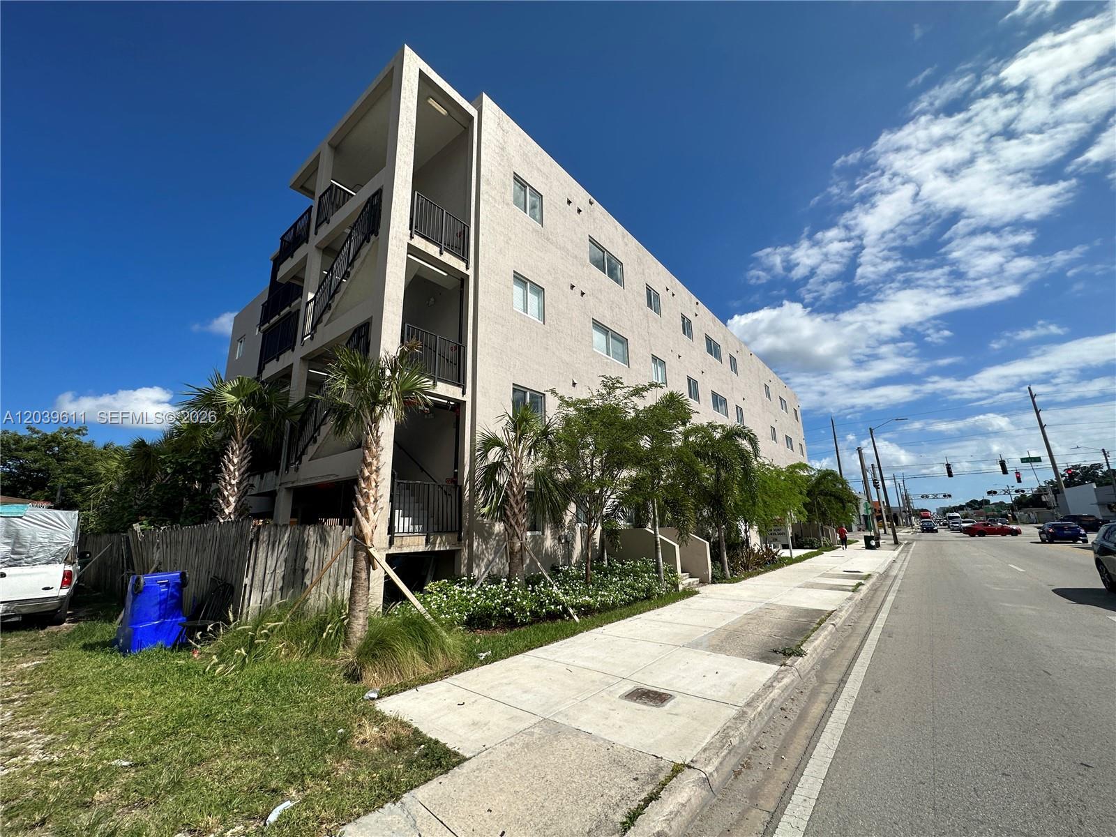 A multi-story apartment building stands next to a sidewalk and a street with traffic — 2311 NW 22nd Ave # 406, Miami FL 33142, MIAMI, FL