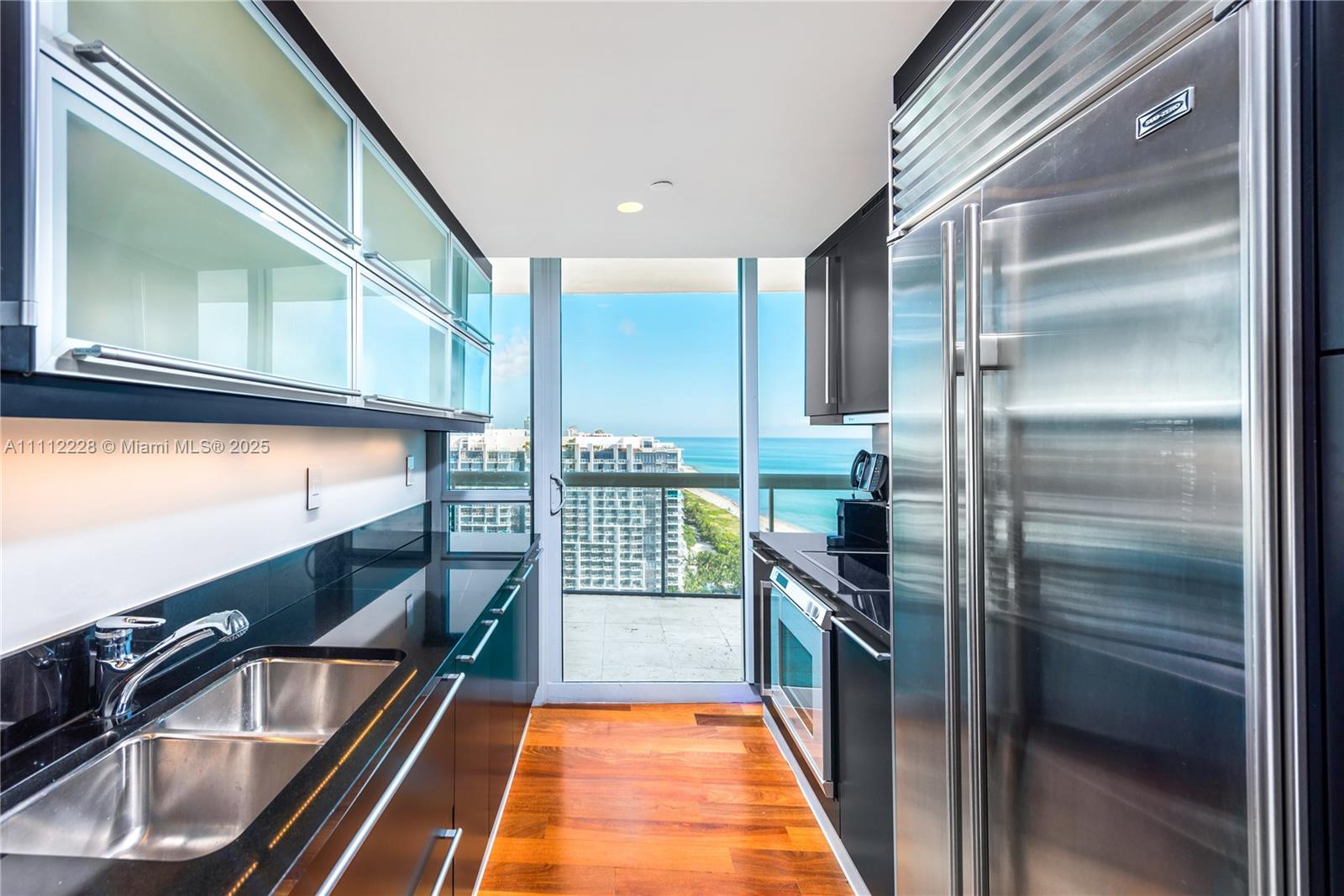 A galley kitchen features dark cabinetry, black countertops, stainless steel appliances, and a balcony view — 101 20th St # 2707, Miami Beach FL 33139, MIAMI BEACH, FL