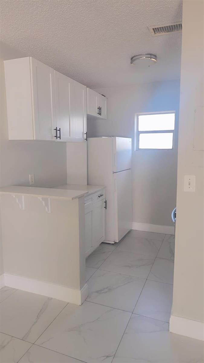 A small kitchen features white cabinets, a white refrigerator, and light-colored marble-patterned tile flooring — 616 NW 5th Avenue # 2, Pompano Beach FL 33060, POMPANO BEACH, FL