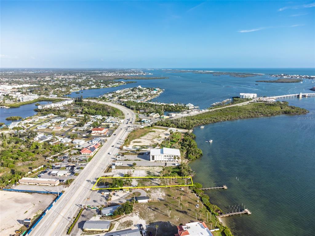 An aerial view shows a vacant waterfront lot outlined in yellow along a coastal highway — 1144 S MCCALL ROAD, ENGLEWOOD, FL