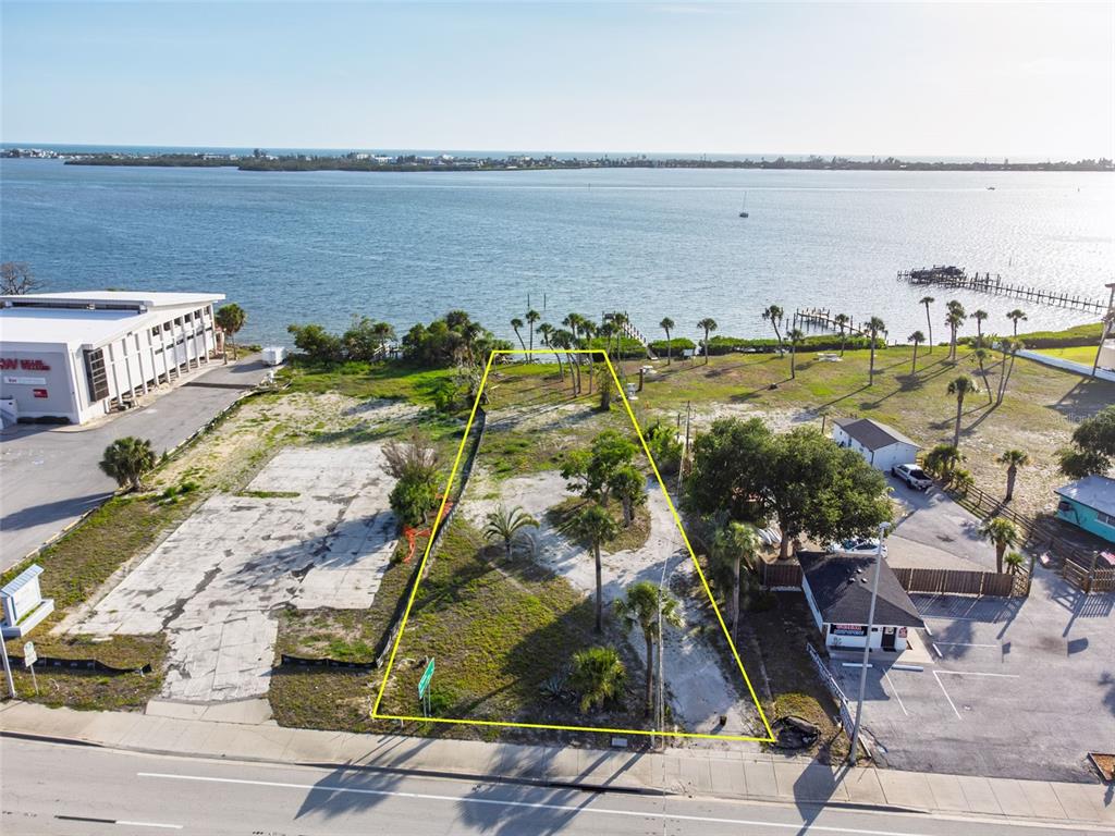 An aerial view shows a vacant, trapezoidal waterfront lot outlined in yellow along a road — 1144 S MCCALL ROAD, ENGLEWOOD, FL