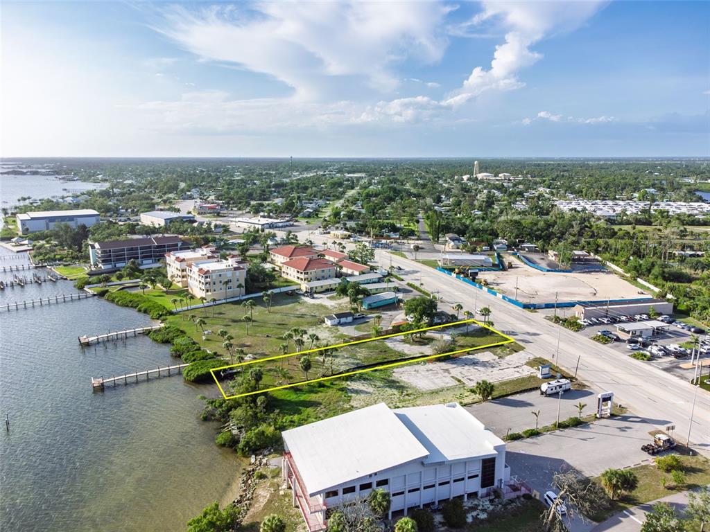 An aerial view shows a vacant waterfront lot outlined in yellow near a coastal road — 1144 S MCCALL ROAD, ENGLEWOOD, FL