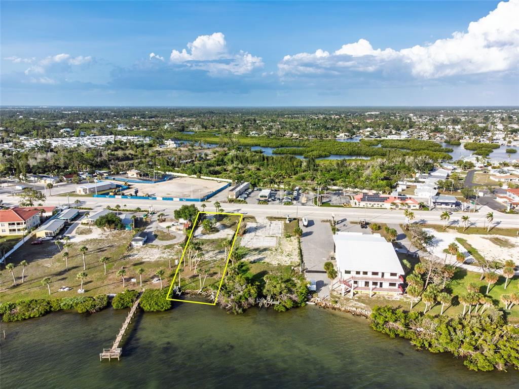 An aerial view shows a vacant waterfront lot outlined in yellow near a road — 1144 S MCCALL ROAD, ENGLEWOOD, FL