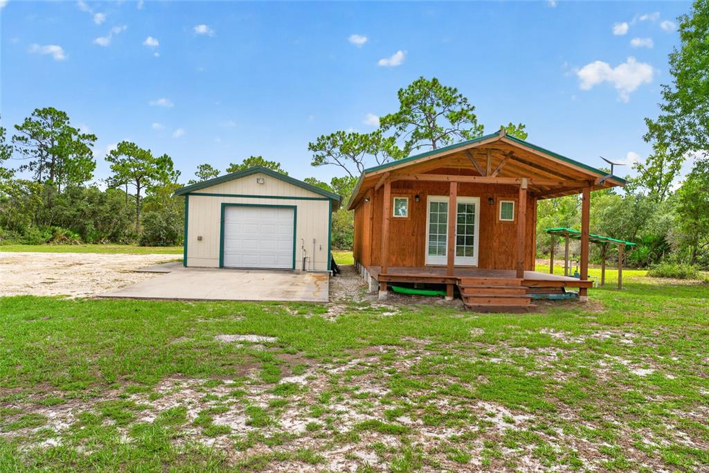 A wooden cabin with a front porch stands next to a detached garage on a lot — 10550 SW 52ND PLACE, CEDAR KEY, FL