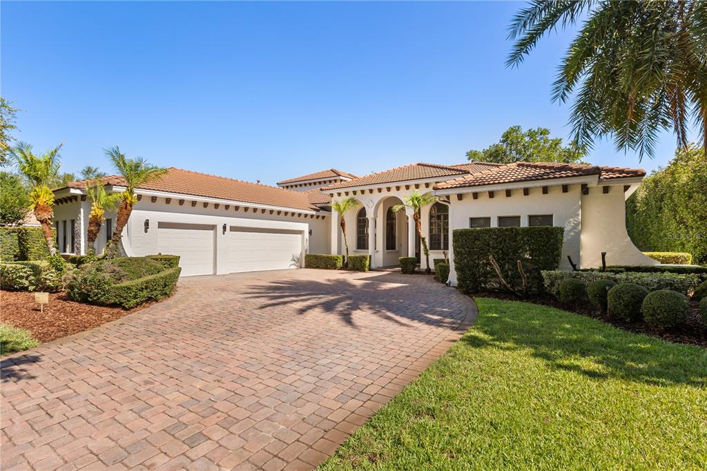 A single-story stucco house with a tile roof, three-car garage, and a brick paver driveway — 11015 HAWKSHEAD COURT, WINDERMERE, FL