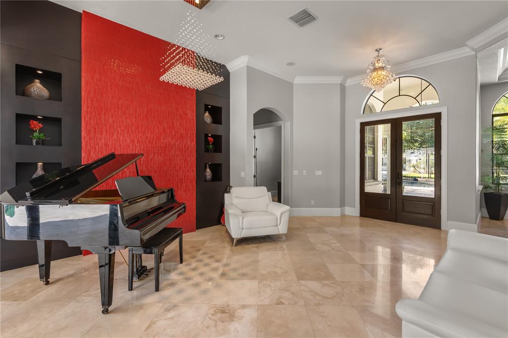 A grand piano sits in a tiled room featuring a red accent wall and white chairs — 11015 HAWKSHEAD COURT, WINDERMERE, FL