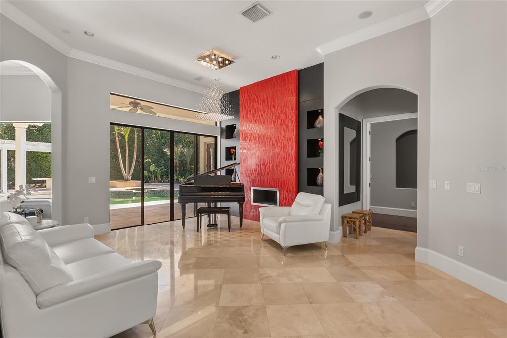 A living room features a grand piano, a red fireplace wall, and white leather furniture — 11015 HAWKSHEAD COURT, WINDERMERE, FL