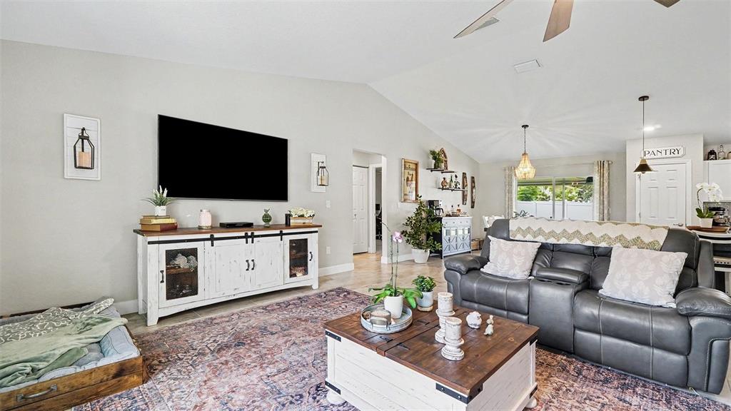 A living room features a large television, white media console, gray sofa, and area rug — 6548 SW 131ST PLACE, OCALA, FL