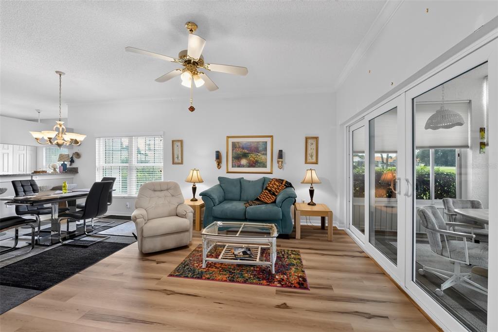 A living room with light wood flooring, a blue sofa, a recliner, and sliding glass doors — 4706 SAND TRAP STREET CIRCLE E UNIT 101, BRADENTON, FL