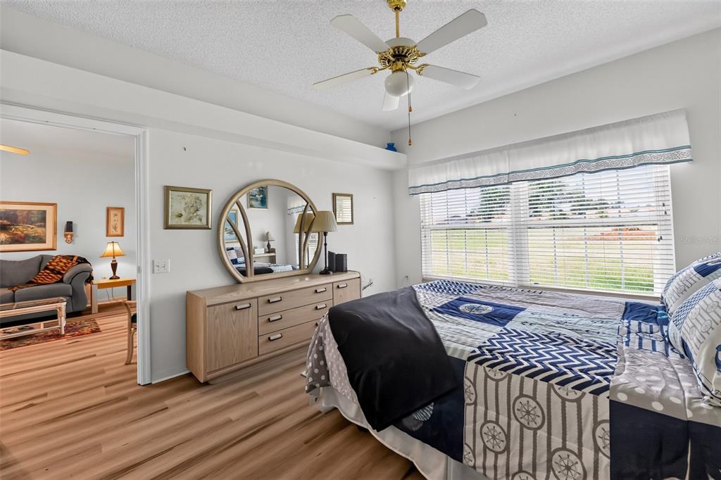 A bedroom with light wood flooring, a ceiling fan, a dresser with a mirror, and bedding — 4706 SAND TRAP STREET CIRCLE E UNIT 101, BRADENTON, FL