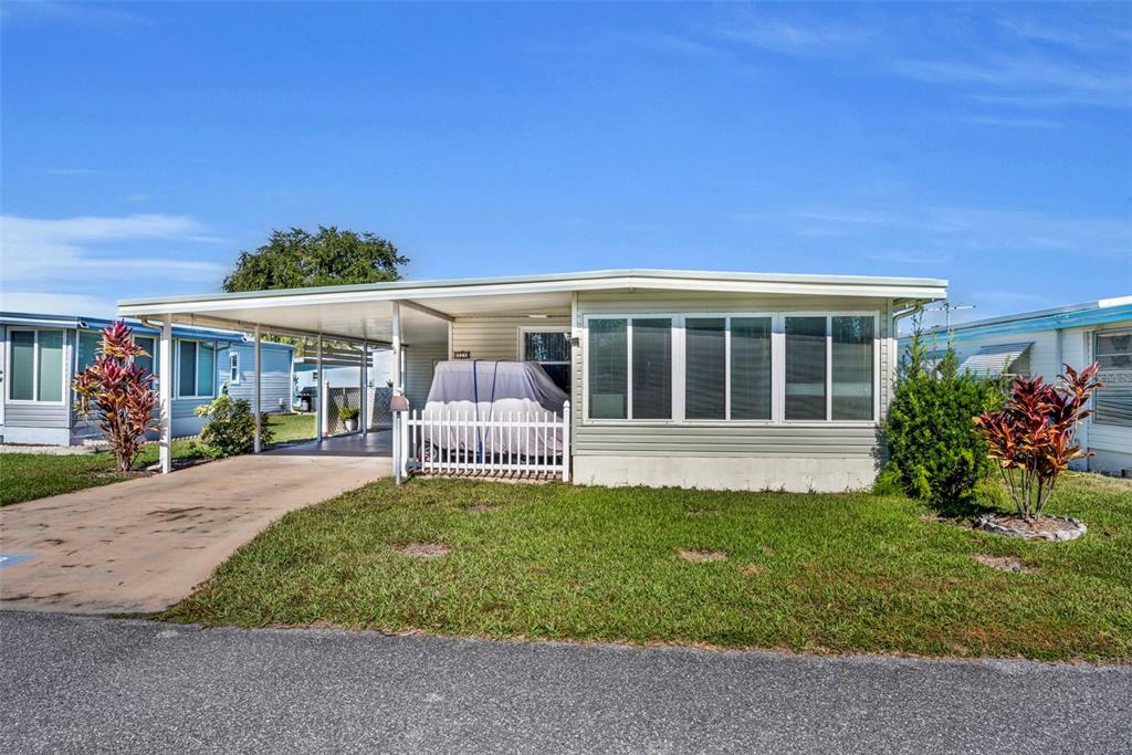 A single-story mobile home with a carport, white picket fence, and large front windows — 223 PARADISE S, LEESBURG, FL