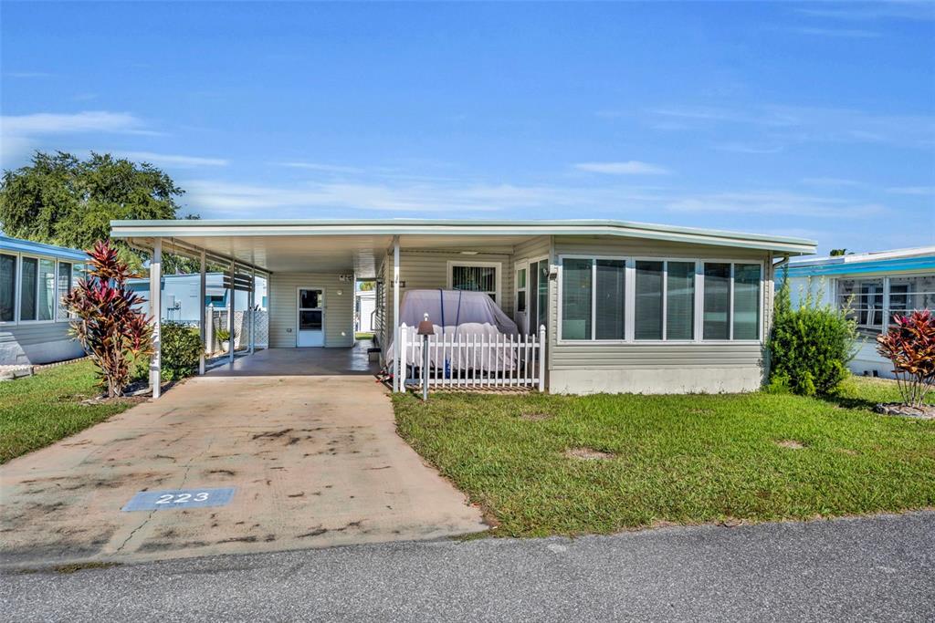 A single-story mobile home with a carport, white siding, and a covered front porch area — 223 PARADISE S, LEESBURG, FL