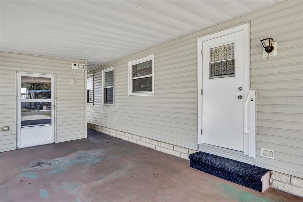 A covered concrete patio features light-colored horizontal siding, two white doors, and two windows — 223 PARADISE S, LEESBURG, FL