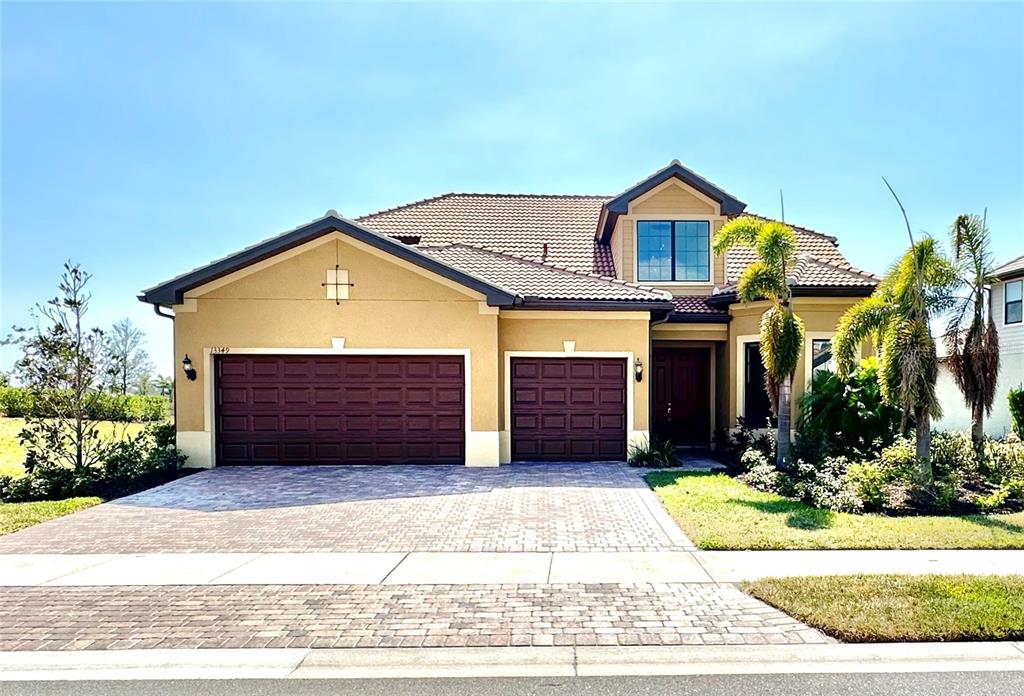 A tan, two-story house features a three-car garage, a tiled roof, and a paved driveway — 13349 VERANDI STREET, VENICE, FL