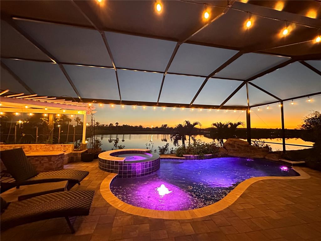 A screened-in patio features a pool, a hot tub, and lounge chairs overlooking a lake — 13349 VERANDI STREET, VENICE, FL