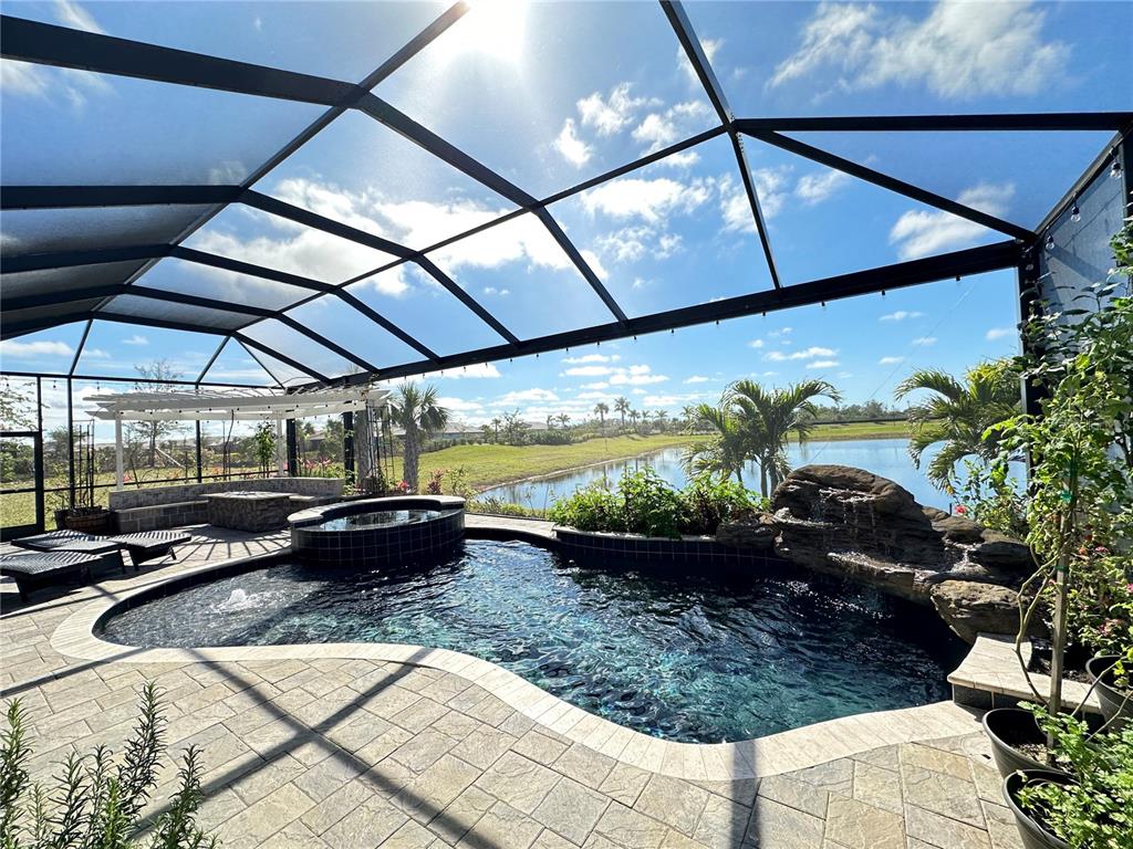 A screened-in pool area features a rock waterfall, a spa, and a view of a lake — 13349 VERANDI STREET, VENICE, FL