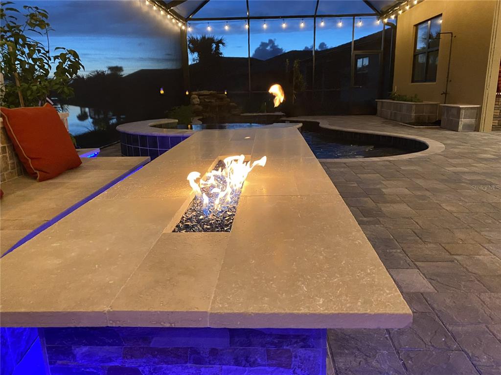 A patio features a stone fire table, a pool, and a spa under a screened enclosure — 13349 VERANDI STREET, VENICE, FL