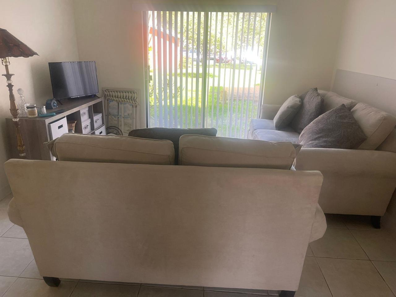A living room features two beige sofas, a television on a stand, and vertical window blinds — 50 SE 12th Street # 145, Boca Raton FL 33432, BOCA RATON, FL