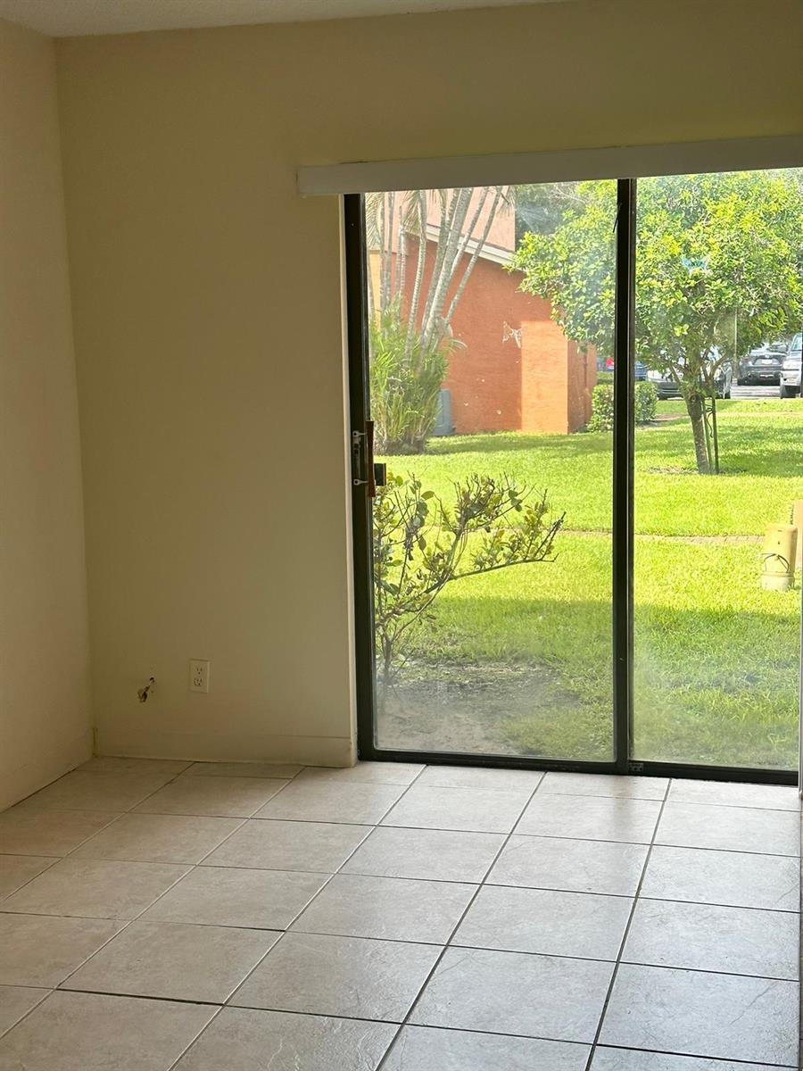 An interior room with beige tile flooring and a sliding glass door leading outside — 50 SE 12th Street # 145, Boca Raton FL 33432, BOCA RATON, FL