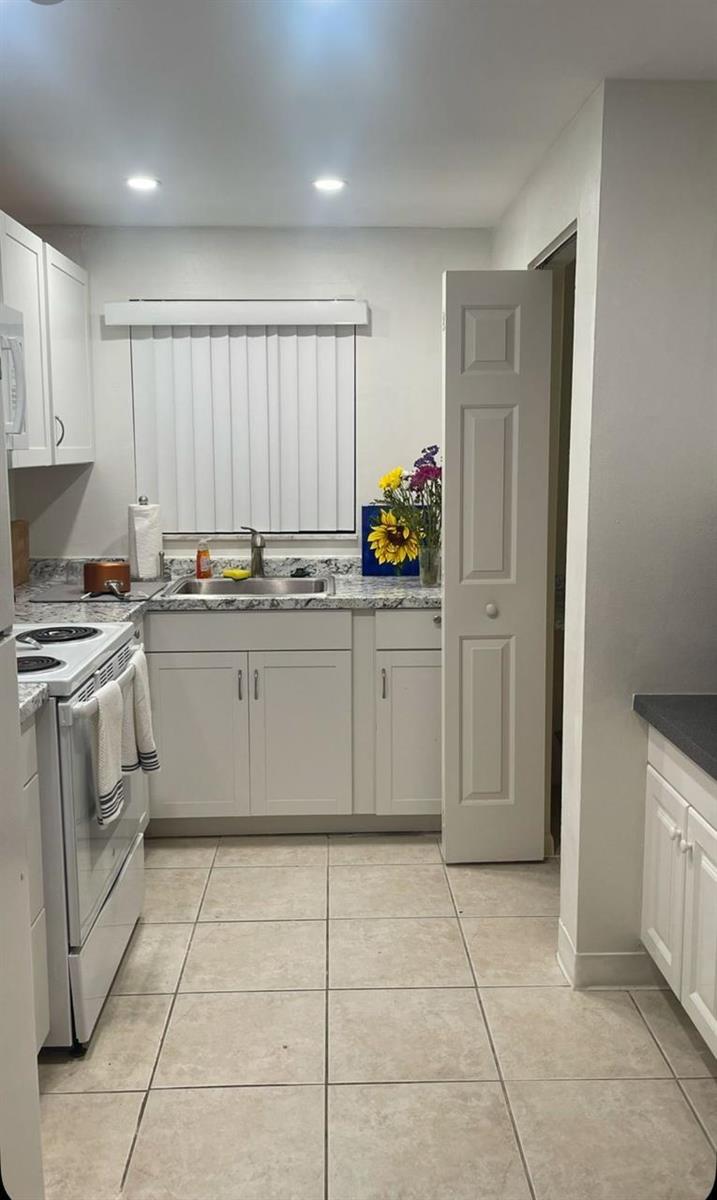 A kitchen with white cabinets, granite countertops, a white stove, and light-colored tile flooring — 50 SE 12th Street # 145, Boca Raton FL 33432, BOCA RATON, FL